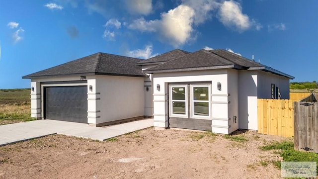 view of front of house featuring fence, roof with shingles, driveway, stucco siding, and a garage