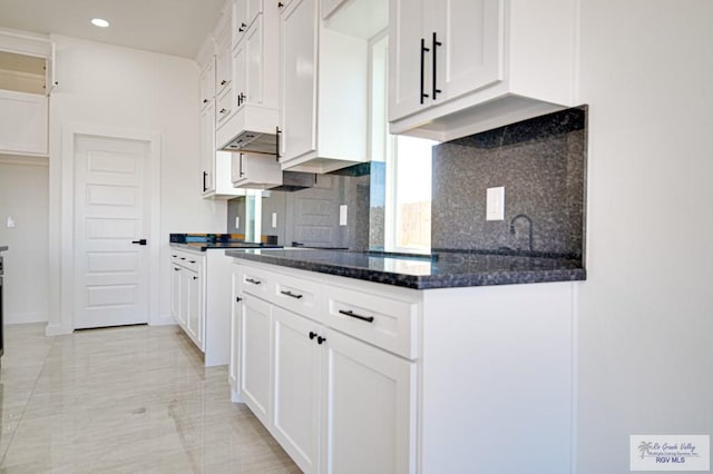 kitchen with under cabinet range hood, tasteful backsplash, white cabinetry, recessed lighting, and dark stone counters