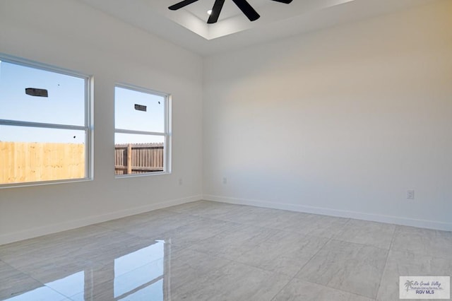 spare room with a tray ceiling, baseboards, and ceiling fan