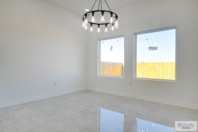 spare room featuring a chandelier, baseboards, and a wealth of natural light