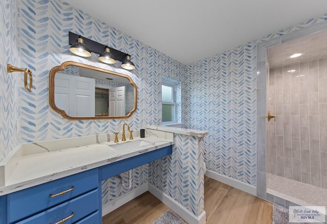 full bathroom with wallpapered walls, baseboards, walk in shower, wood finished floors, and vanity