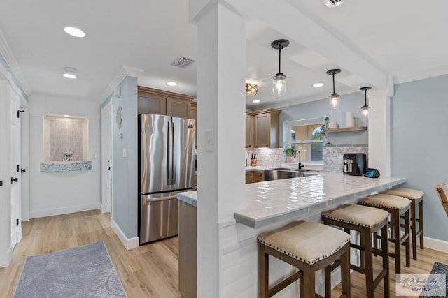 kitchen featuring visible vents, ornamental molding, a sink, a kitchen breakfast bar, and freestanding refrigerator