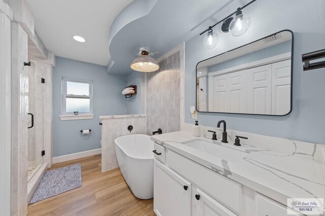 bathroom with a freestanding tub, wood finished floors, a stall shower, and vanity