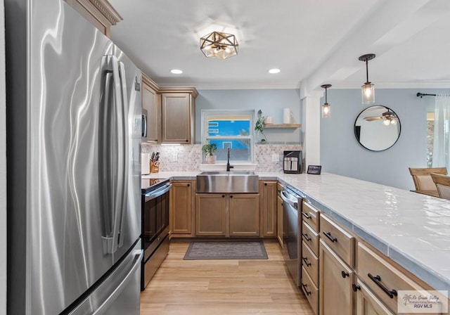 kitchen featuring light wood-type flooring, light countertops, ornamental molding, appliances with stainless steel finishes, and a sink