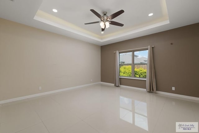 tiled empty room with a raised ceiling and ceiling fan