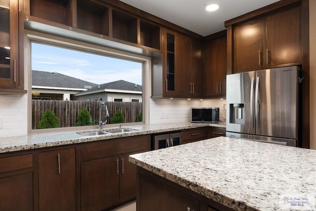 kitchen with stainless steel refrigerator with ice dispenser, sink, tasteful backsplash, light stone counters, and dark brown cabinets