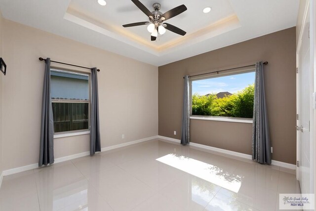 tiled spare room featuring ceiling fan and a tray ceiling