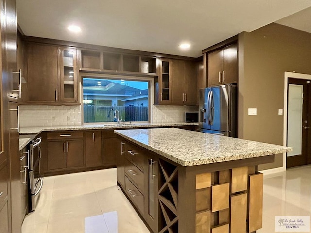 kitchen with sink, stainless steel fridge, a kitchen breakfast bar, a center island, and light stone countertops