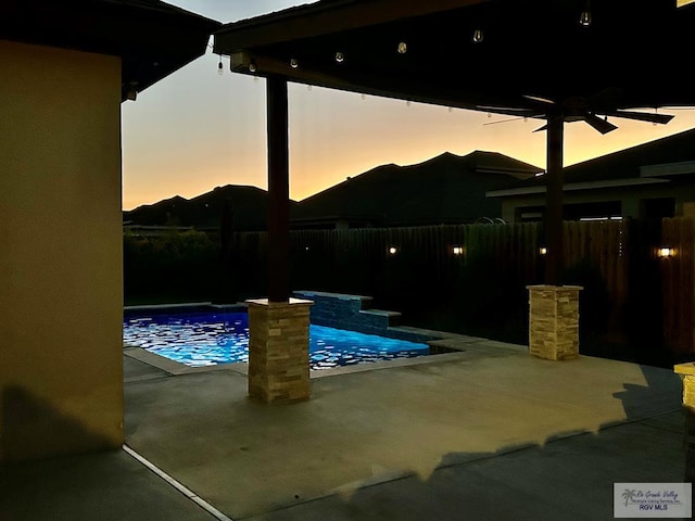 pool at dusk with a patio and ceiling fan