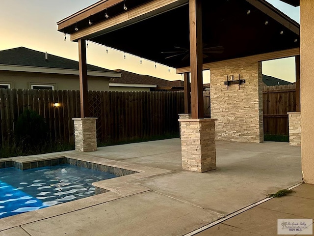 pool at dusk featuring ceiling fan and a patio