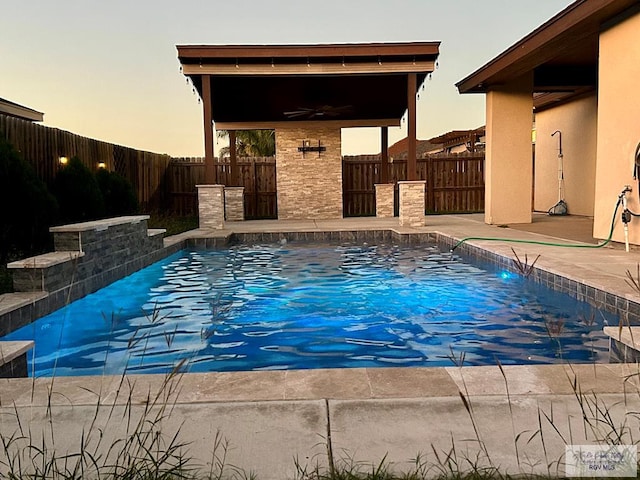 pool at dusk featuring a patio area, pool water feature, and ceiling fan