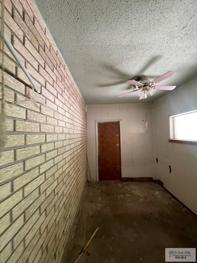 interior space with ceiling fan, a textured ceiling, and brick wall