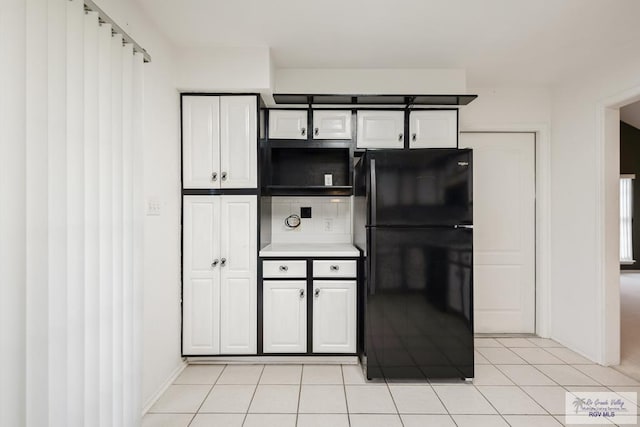 kitchen featuring white cabinets, light tile patterned flooring, and black fridge