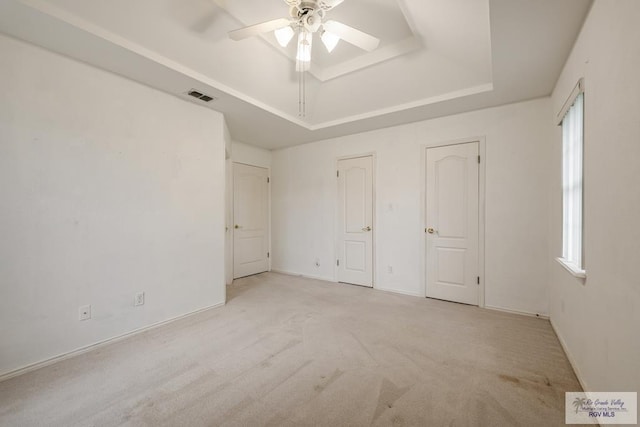 unfurnished bedroom with a raised ceiling, ceiling fan, and light carpet