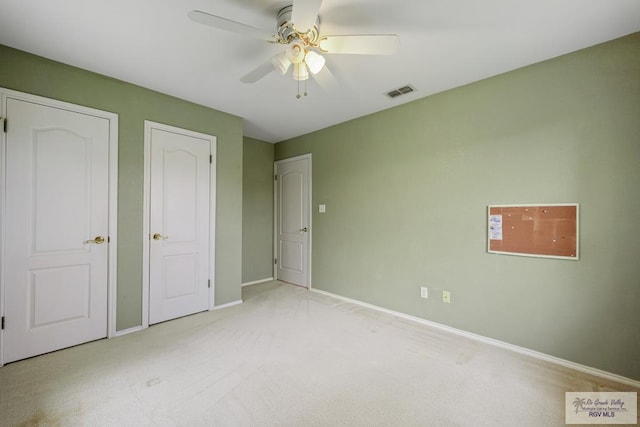 unfurnished bedroom with light carpet, two closets, and ceiling fan