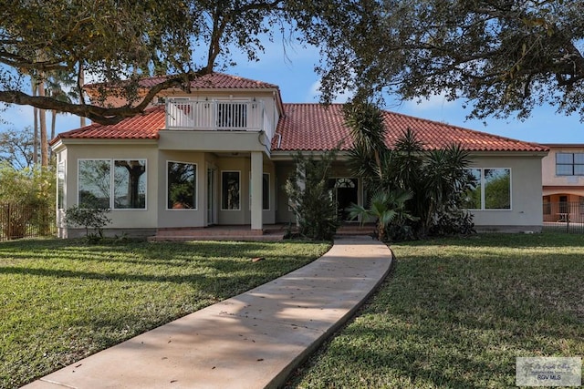 mediterranean / spanish house featuring a tiled roof, a front yard, and a balcony