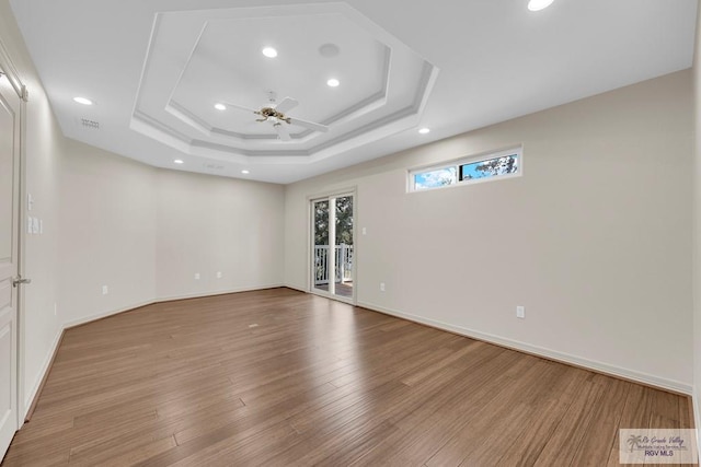 unfurnished room featuring a tray ceiling, baseboards, wood finished floors, and a ceiling fan