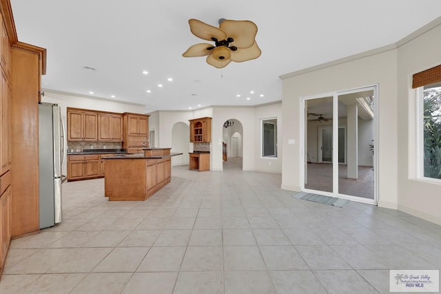 kitchen featuring dark countertops, tasteful backsplash, ceiling fan, freestanding refrigerator, and arched walkways