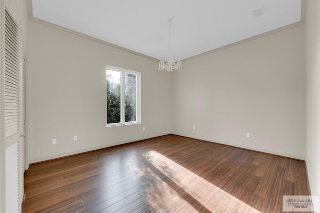 empty room featuring a chandelier, ornamental molding, baseboards, and wood finished floors