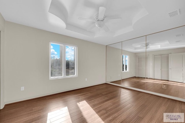 unfurnished room featuring baseboards, visible vents, a tray ceiling, ceiling fan, and wood-type flooring