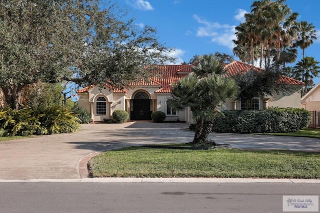 mediterranean / spanish-style home with decorative driveway, a front yard, stucco siding, and a tiled roof