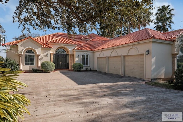 mediterranean / spanish-style home featuring a tile roof, an attached garage, driveway, and stucco siding