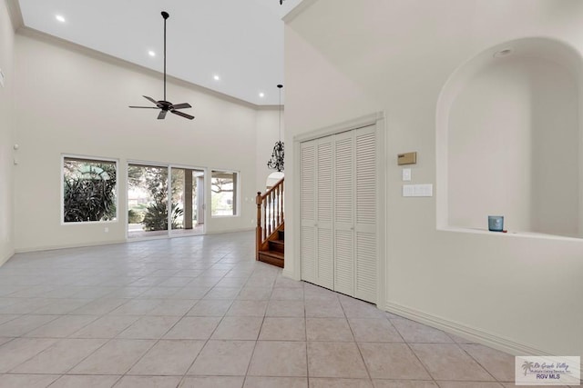 interior space with stairway, light tile patterned floors, a ceiling fan, baseboards, and a high ceiling