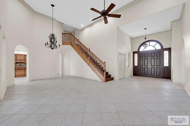 foyer featuring baseboards, arched walkways, a towering ceiling, crown molding, and ceiling fan with notable chandelier