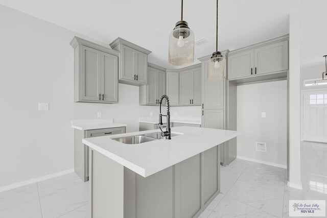 kitchen with hanging light fixtures, an island with sink, sink, and gray cabinetry