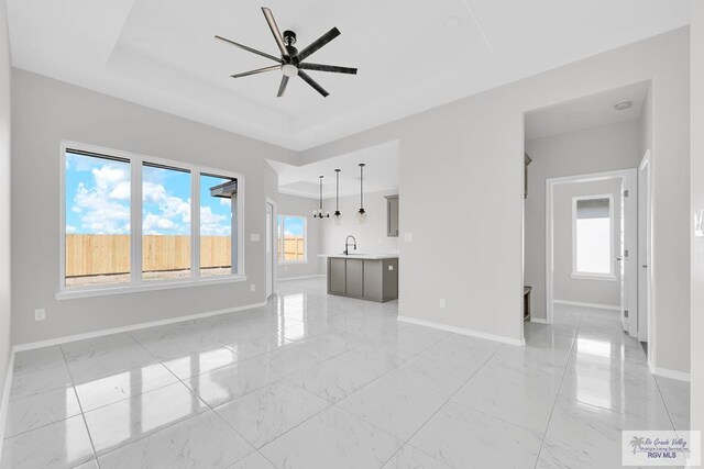 unfurnished living room featuring a healthy amount of sunlight, a tray ceiling, and ceiling fan