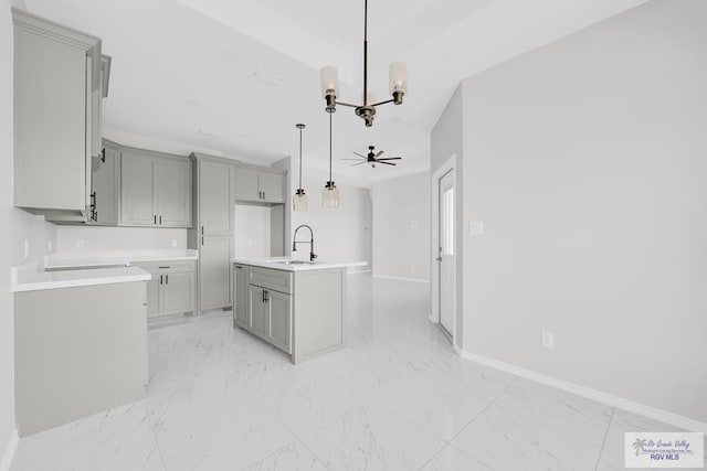 kitchen with a center island with sink, hanging light fixtures, ceiling fan with notable chandelier, gray cabinets, and sink