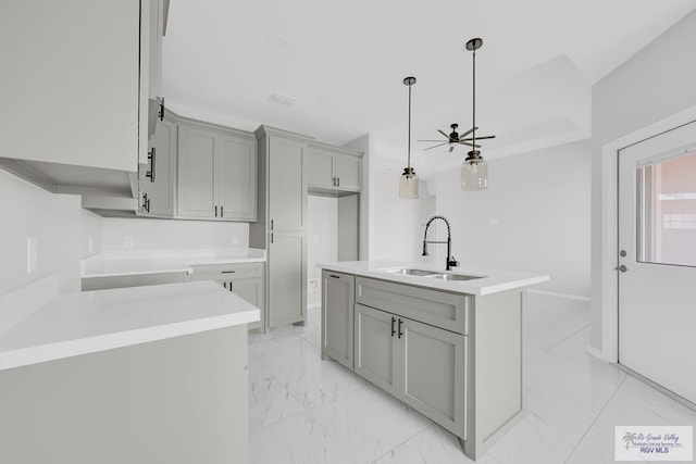 kitchen featuring a center island with sink, decorative light fixtures, ceiling fan, gray cabinets, and sink