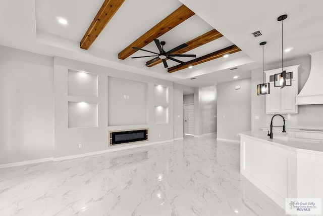 unfurnished living room featuring beam ceiling, ceiling fan, and sink