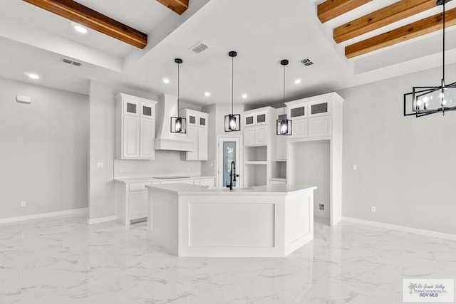 kitchen with custom range hood, a center island with sink, beamed ceiling, white cabinetry, and hanging light fixtures