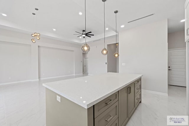 kitchen featuring a raised ceiling, a kitchen island, decorative light fixtures, and ceiling fan with notable chandelier