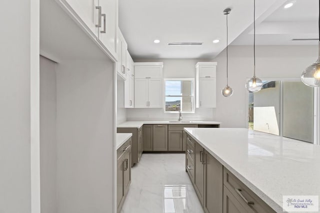 kitchen with light stone countertops, stainless steel fridge, sink, white cabinets, and hanging light fixtures