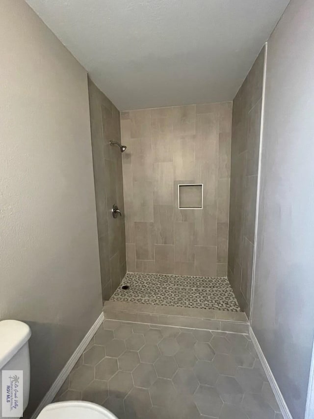 bathroom with tiled shower, tile patterned flooring, and toilet