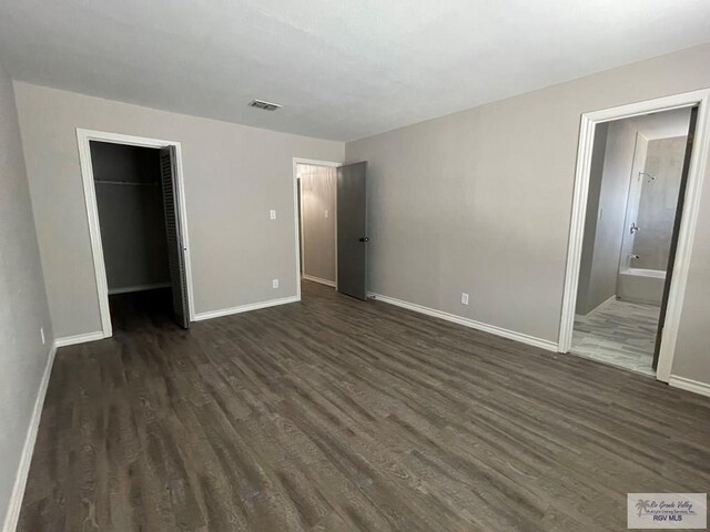 unfurnished bedroom featuring ensuite bath, a spacious closet, a closet, and dark hardwood / wood-style floors