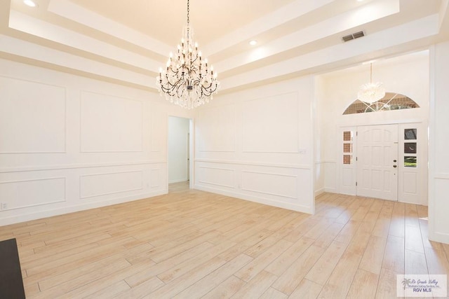 entrance foyer featuring a raised ceiling, hardwood / wood-style floors, and an inviting chandelier