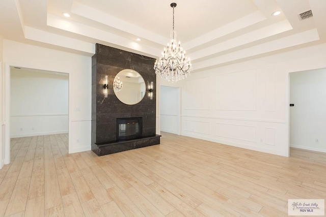 unfurnished living room featuring an inviting chandelier, a fireplace, a raised ceiling, and light wood-type flooring