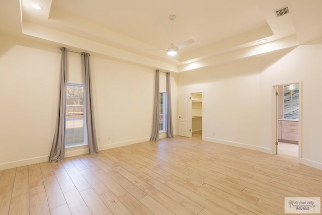 unfurnished room featuring ceiling fan, light wood-type flooring, and a tray ceiling