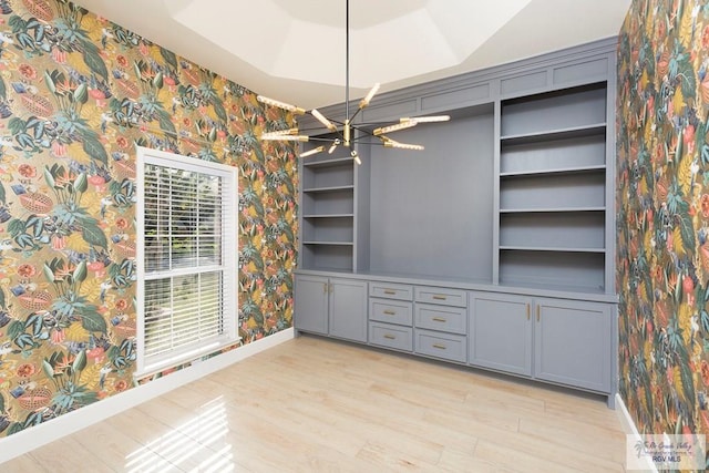 unfurnished dining area with a notable chandelier, light wood-type flooring, and a tray ceiling