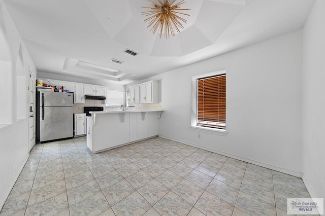 4217 W Ithaca Ave, Mcallen, TX 78501 - kitchen with freestanding refrigerator, a tray ceiling, a peninsula, under cabinet range hood, and plenty of natural light