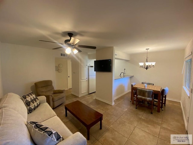 living area featuring light tile patterned floors, baseboards, visible vents, and ceiling fan with notable chandelier