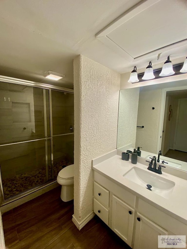 bathroom featuring a textured wall, toilet, vanity, a shower stall, and wood finished floors