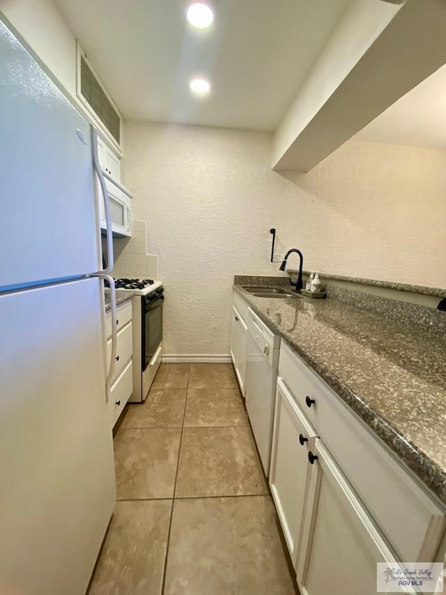 kitchen featuring visible vents, white cabinets, a sink, dark stone countertops, and white appliances