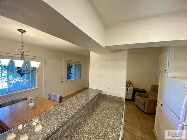 kitchen with pendant lighting, a textured wall, an inviting chandelier, freestanding refrigerator, and tile patterned floors