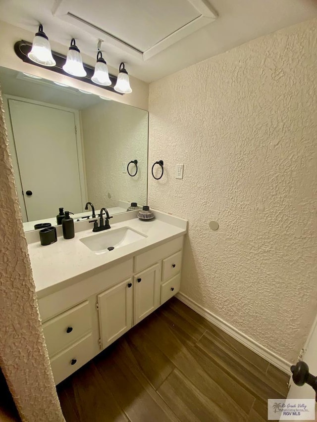 bathroom with vanity, baseboards, wood finished floors, and a textured wall