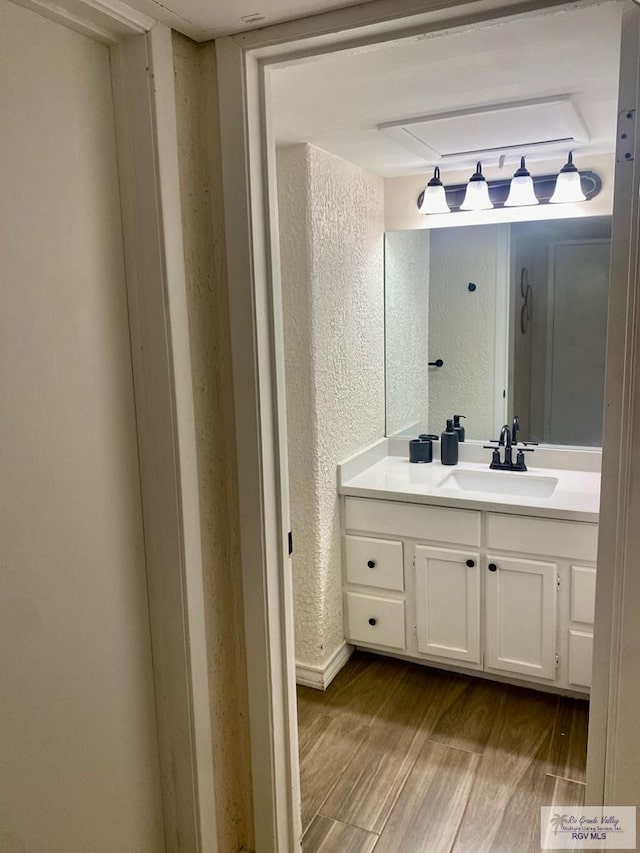 bathroom with a textured wall, vanity, and wood finished floors