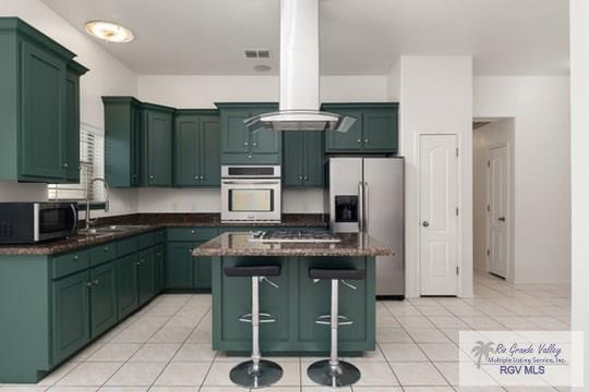 18186 King Palm Dr, Harlingen, TX 78552 - kitchen featuring appliances with stainless steel finishes, green cabinetry, a sink, a kitchen breakfast bar, and light tile patterned flooring